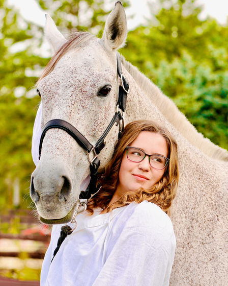 High school senior picture in Minneapolis, MN of a young woman on a farm, standing in front of a tan colored horse. Photography by Bonni Allen.