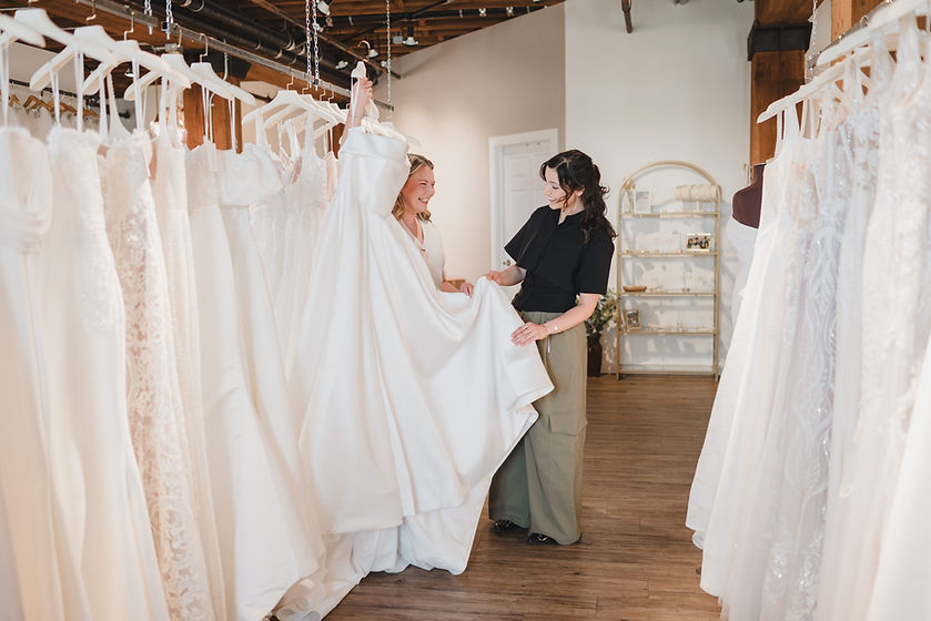 A bride shopping wedding dresses hanging on the racks with the help of a Stylist at Miss Ruby Bridal