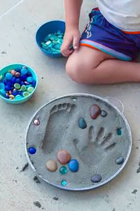 Concrete garden stepping stone with a child's handprint, footprint, and colorful stones