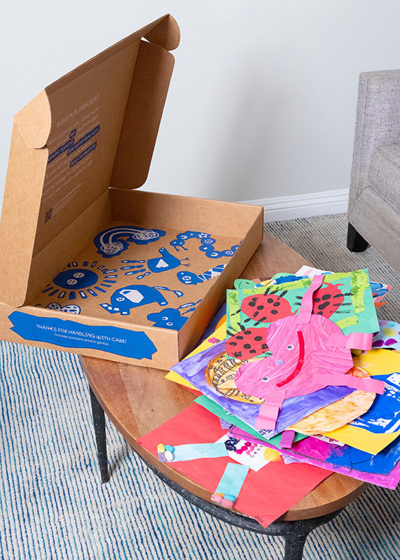Artkive Box on a coffee table next to a pile of kids' artwork ready to be packed into a memory book