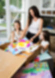A mom packs an Artkive box with her two daughters, preparing to send in their children's artwork to be made into a memory book
