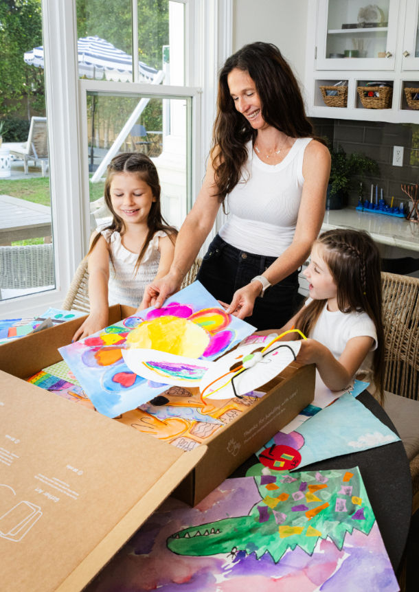 A mom packs an Artkive box with her two daughters, preparing to send in their children's artwork to be made into a memory book