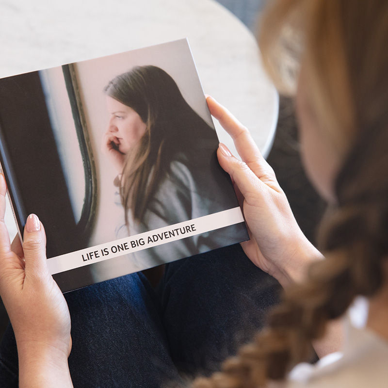 Woman holding an open hardcover Cardkive photo book with the cover reading "Life is one big adventure"