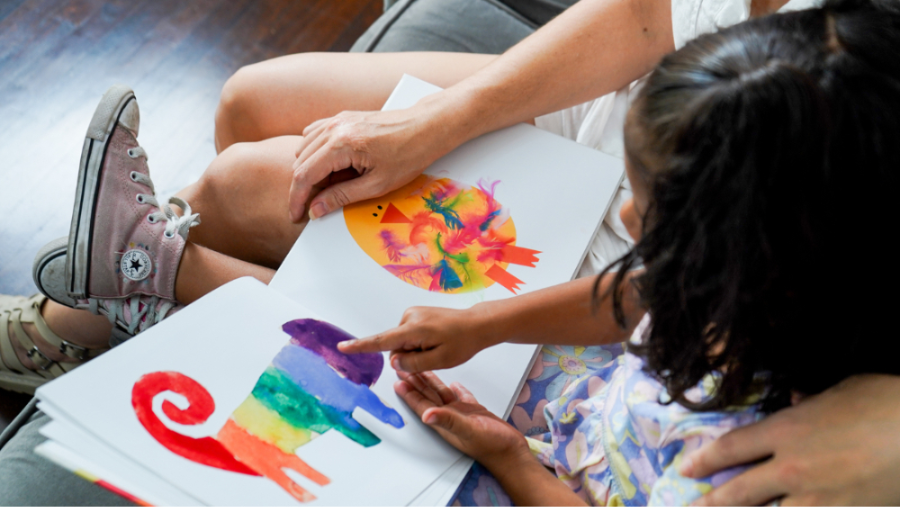 A grandparent is sitting with a small child, looking over a book that child made out of their art. (personalized kids books, gift ideas for grandma gifts for grandma)