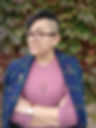 Nonbinary Filipina queer with glasses and an undercut, wearing a blue plaid blazer on their shoulders, cape-style, and dusty pink thermal shirt. Styled with bronze accessories - a vintage sword pin, an indie artist-made shield pin, and a miniature deer skull pendant. This nerd's arms are crossed, a smirk on their face, tryna look like some kind of cool kid.