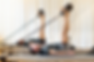 Man in activewear exercises on a Pilates reformer, lifting legs with resistance bands. Bright, curtained setting, focused and calm mood.