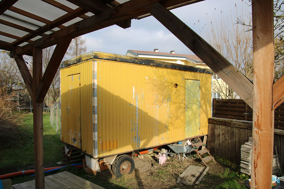 Ein gelber alter Bauwagen steht auf einem Anhänger im Garten. Darin befindet sich das Bade- und Gästezimmer.