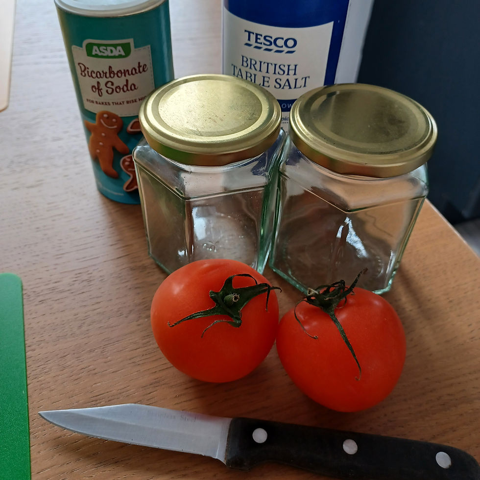 Two tomatoes and a knife on a wooden table. Nearby, two empty jars and containers of baking soda and table salt are visible.