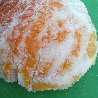 A yellowing mummified tomato, covered in salt lies on a green mat.