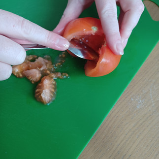 A person scrapes the pulp out of a tomato using a spoon.