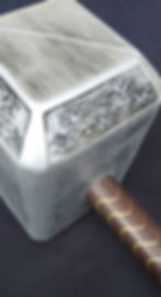 Silver hammer with intricate designs on the head and a brown handle with gold patterns, set against a dark background.