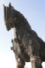 Wooden Trojan horse statue with ropes, set against a clear blue sky. The textured, weathered wood gives a historic and mythical feel.