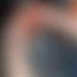 A tomato is washed in water over a black sink.