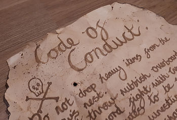 A weathered parchment labeled "Code of Conduct" with a skull and crossbones. Antique handwriting on a wooden surface, aged effect.