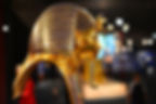 Golden pharaoh mask with blue stripes on display, bokeh lights in background creating a majestic mood.