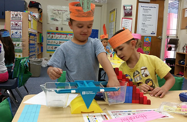 Students engaged in hands-on learning, involving a scale and connecting blocks.