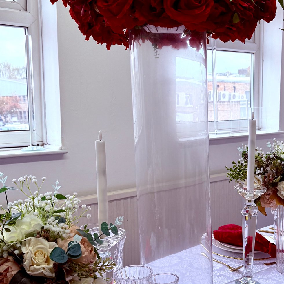 Red roses centerpiece, glass vase, and candles set on decorated table. Admire's Furnishings
