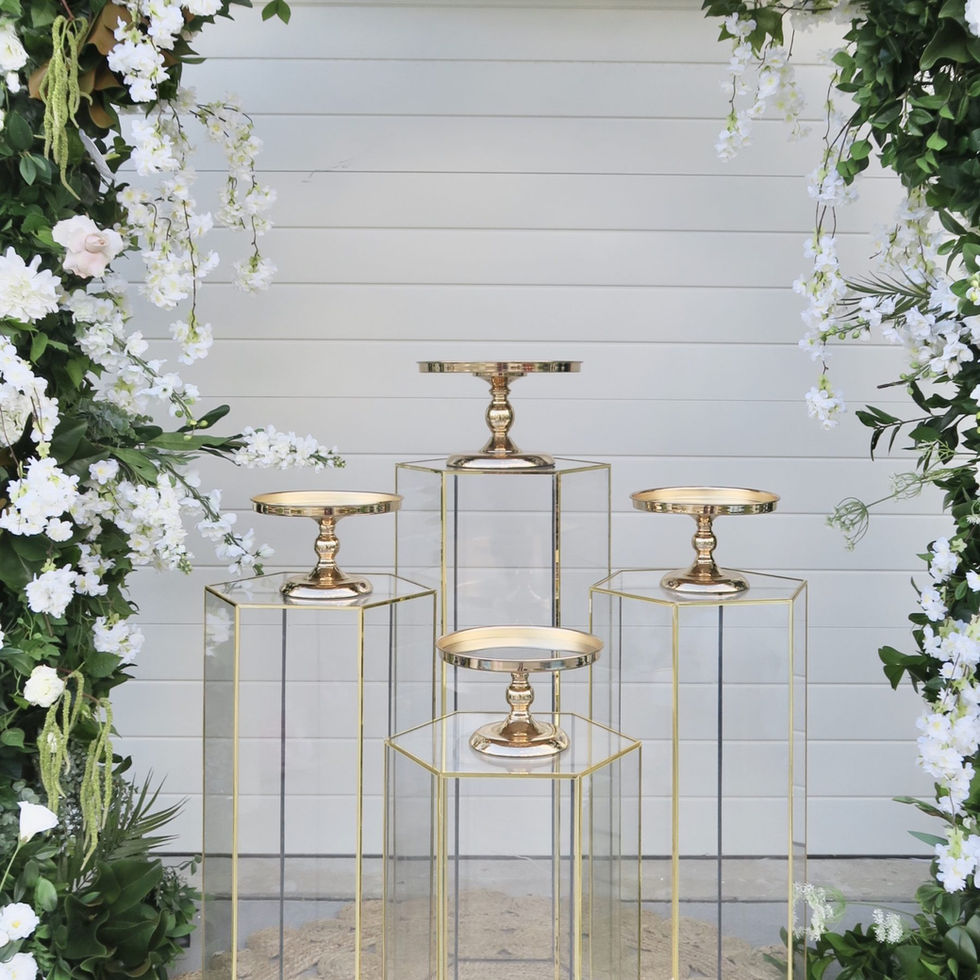 Gold cake stands on glass pedestals, framed by white floral arch