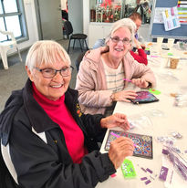 Two women sitting at a table smiling and doing art activity during Ironbark session