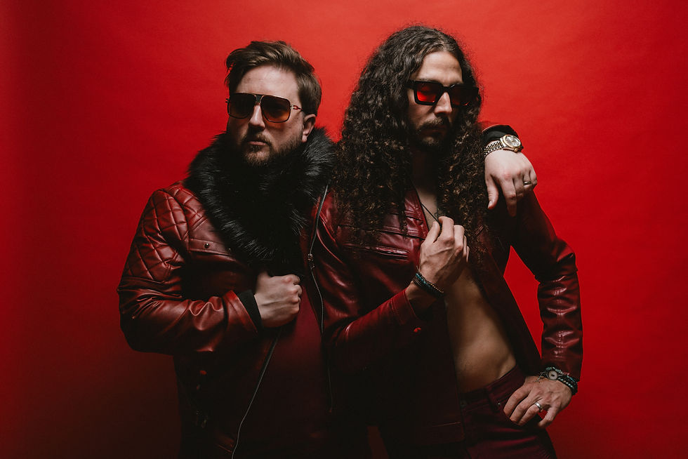 Two men in red leather jackets and sunglasses pose confidently against a red background. One has a fur collar; both exude a cool vibe. HIVESONG - The Cage, a music blog powered by Cage Riot
