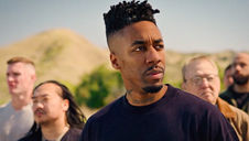 A group of people stands outdoors with a serious expression. Prominent man in foreground has "UNFINISHED" tattoo on neck. Desert background. Dax - The Cage, a music blog powered by Cage Riot