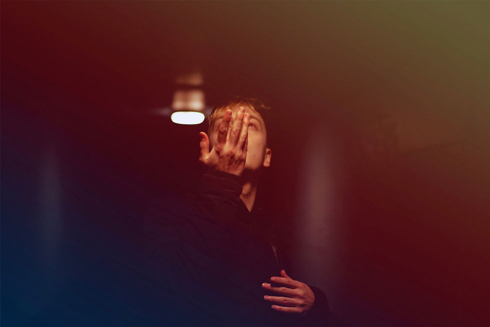 A person in a dark setting covers their face with one hand, light overhead. The scene is dimly lit with a moody, mysterious atmosphere. Marxus - The Cage, a music blog powered by Cage Riot