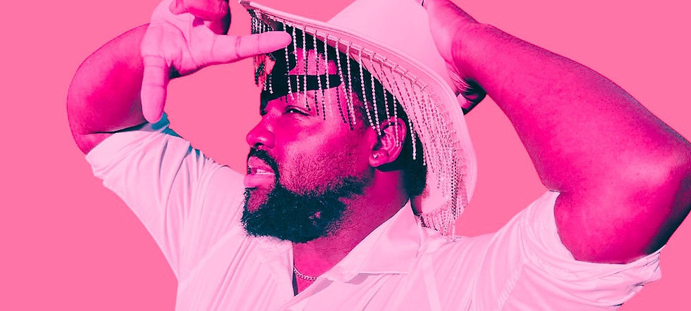 Man wearing a white shirt and cowboy hat with fringe, posing confidently against a pink background. Edgy and vibrant. J Terrell - The Cage, a music blog powered by Cage Riot
