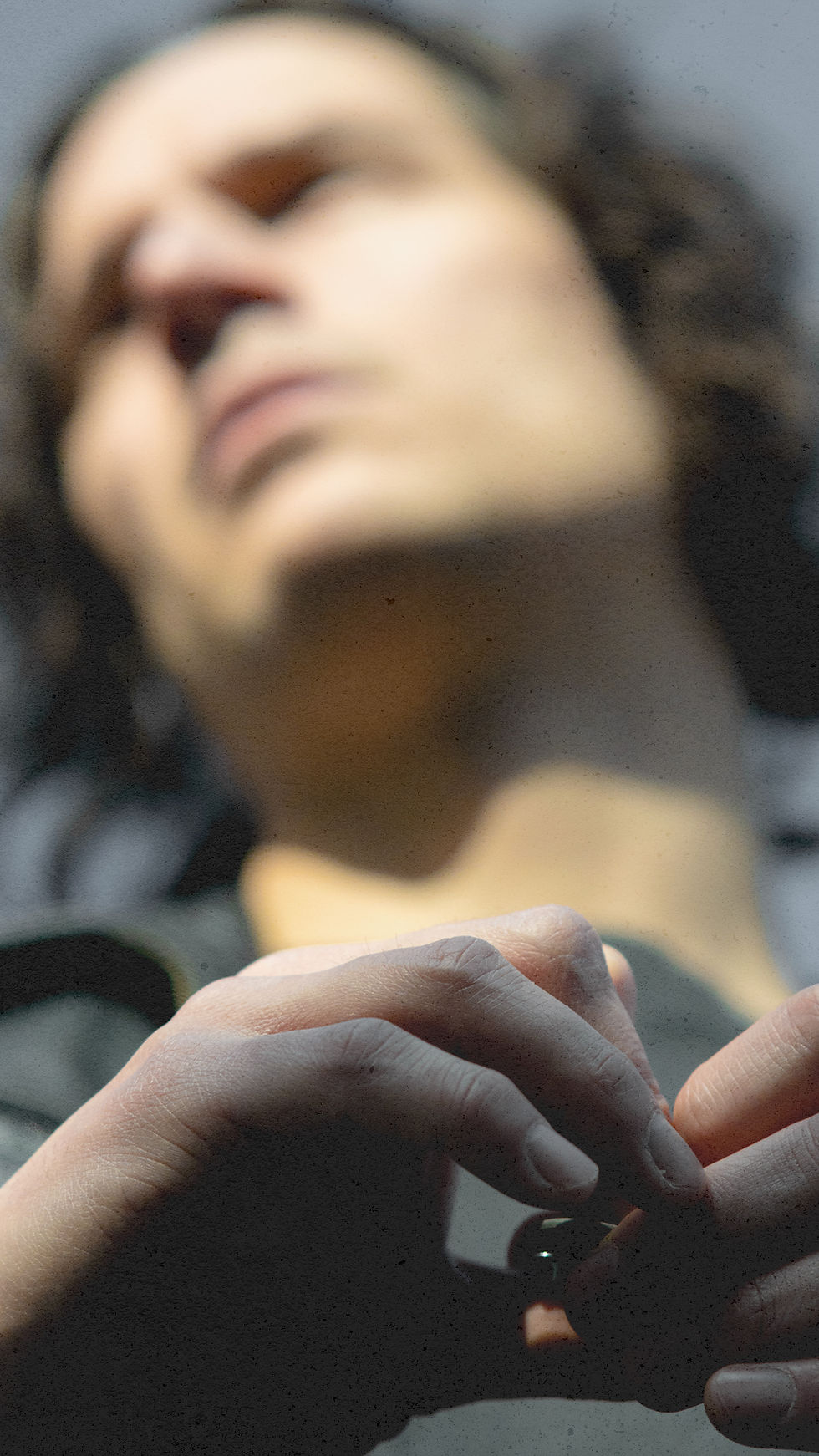 Blurred person in background, focus on hands holding a small object, with soft lighting and a contemplative mood. Neutral color tones. Marc Gundermann’ - The Cage, a music blog powered by Cage Riot
