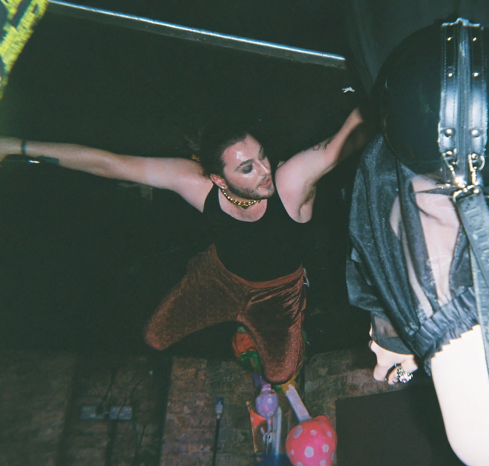 Person in a black tank top and red pants poses dynamically in a dimly lit setting with balloons and brick wall, exuding a dramatic vibe. Carδamo - The Cage, a music blog powered by Cage Riot