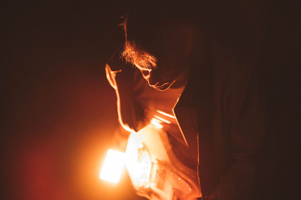 A person plays an electric guitar illuminated by an orange light in a dark setting, creating a moody and dramatic atmosphere. Galaxy Club - The Cage, a music blog powered by Cage Riot
