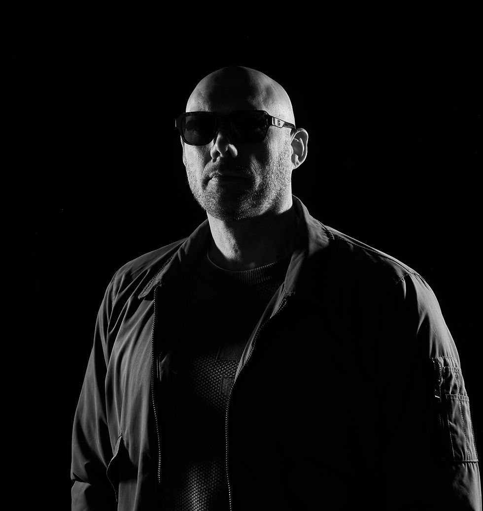 Bald man in sunglasses and jacket stands in dark setting, lit dramatically from the side, creating a shadowed, mysterious atmosphere. mindwax - The Cage, a music blog powered by Cage Riot