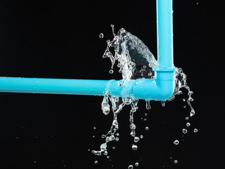 Blue PVC pipes with a leaking joint, splashing water against a black background. Water droplets are visibly spraying outward.