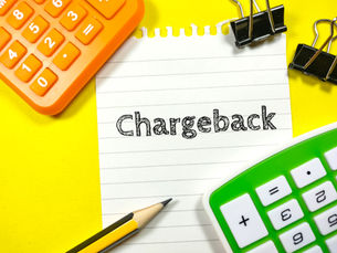 Orange and green calculators, pencil, and paper clip on yellow background. Note reads "Chargeback," suggesting a financial theme.
