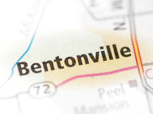 Close-up of a map highlighting Bentonville with bold black text. Thin colored lines and nearby roads are visible. Softly blurred background.