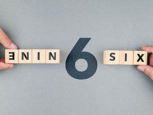Hands hold wooden blocks spelling NINE and SIX around a large 6 on a gray background.