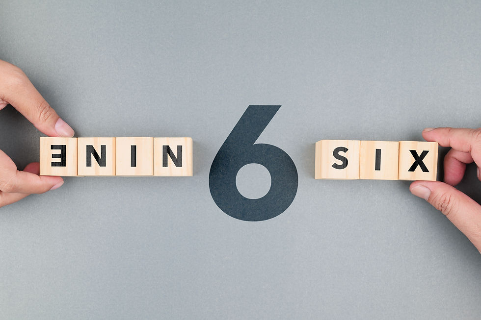 Hands hold wooden blocks spelling NINE and SIX around a large 6 on a gray background.