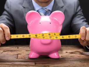Pink piggy bank squeezed by a measuring tape.