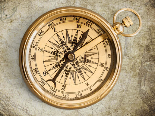 A vintage brass compass on a weathered map background. The compass features intricate black markings and points north. Subtle, nostalgic mood.
