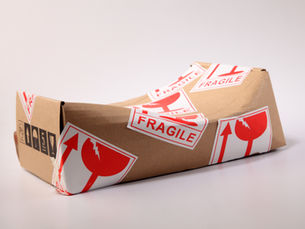 A dented cardboard box covered in red "FRAGILE" stickers is set against a plain white background, conveying a sense of mishandling.