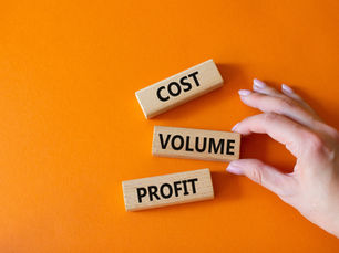 Wooden blocks labeled COST, VOLUME, PROFIT on orange background. A hand adjusts the VOLUME block, suggesting analysis or strategy.