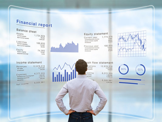 Man in striped shirt examines financial reports and graphs on a transparent screen. Data includes balance sheets and performance metrics.
