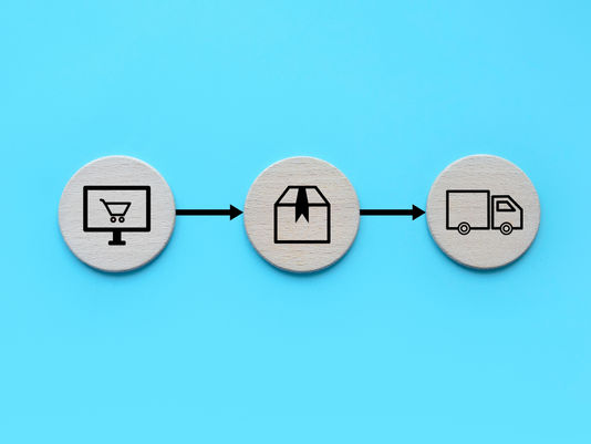 Three wooden discs on a blue background depict online shopping: a screen, package, and delivery truck, connected by arrows.