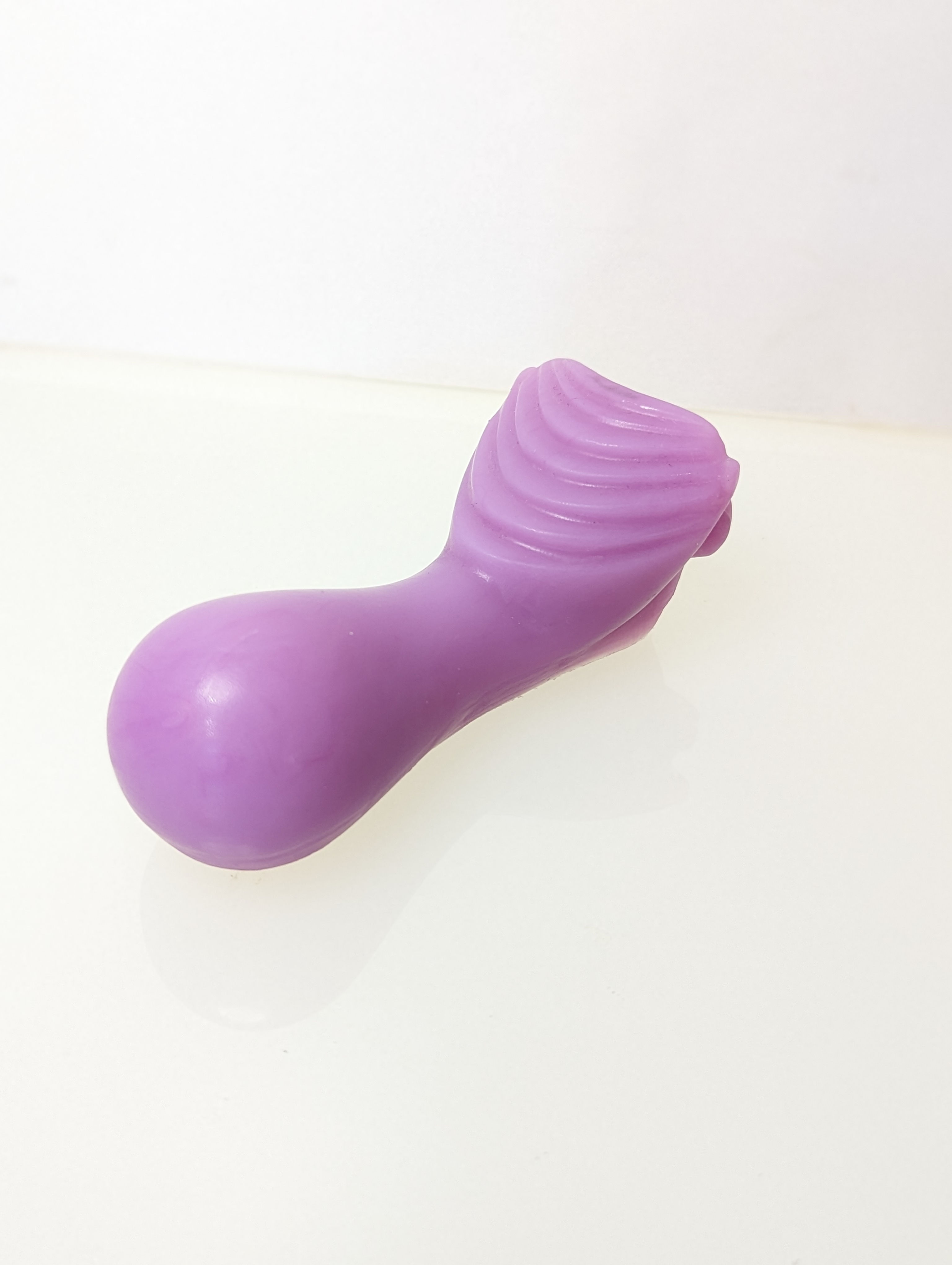 Isometric view of a purple silicon ride on grinder with inclined ridge facing up, bulbous end, and a dip for pubic comfort