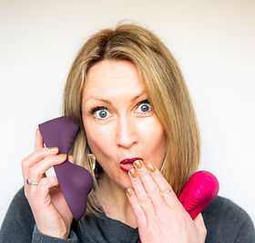 Tabitha Rayne, Ruby Glow inventor making a cheeky exprssin as she holds two RubyGlow sex toys up, one as if it is a telephone