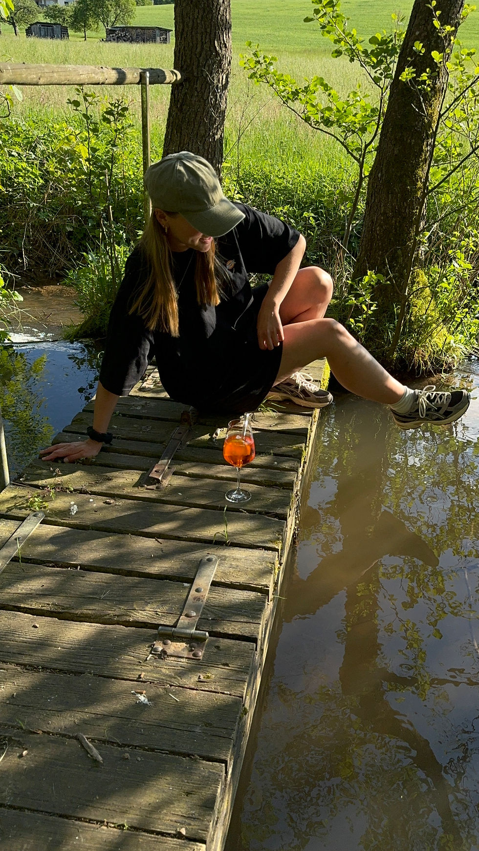 Eine Frau, die am Steg sitzt und Aperol trinkt