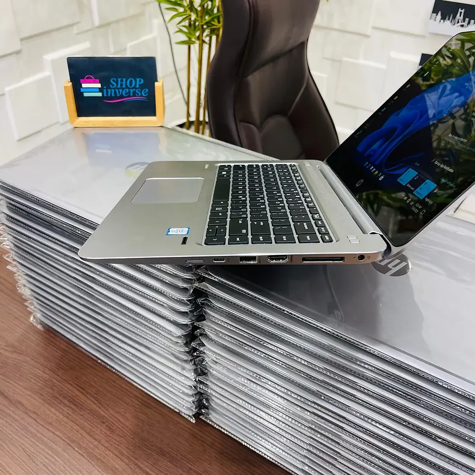 Silver laptop on display, open with screen on, resting on a stack of closed laptops. A sign reads "SHOPinverse" in the background.