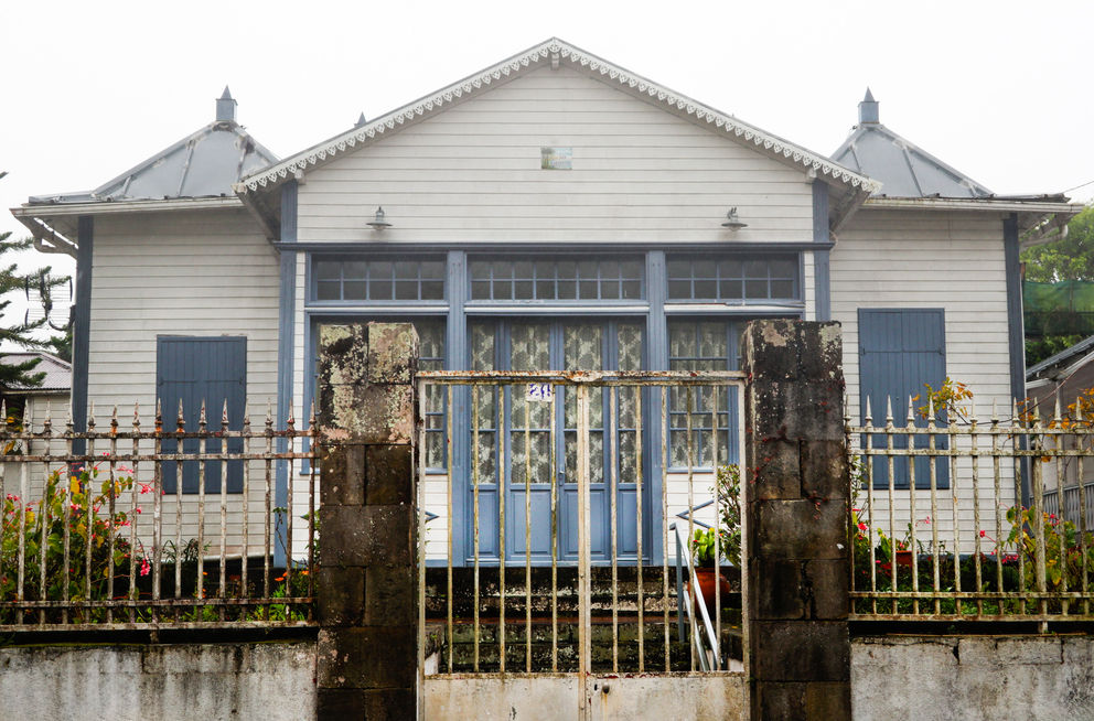 Passer un week-end à Hell-Bourg, c'est comme faire un bond dans le temps en matière d'architecture notamment. En cette période hivernale, entre deux gouttes de pluie, le soleil illumine les rues de ce village créole situé au flanc du cirque de Salazie. Située près de l'église, la Maison Folio, inscrite au titre des Monuments Historiques depuis 1989, permet une plongée dans l'Histoire de La Réunion, dans l’histoire de ces bourgeois qui montaient au village pour faire une cure thermale et se reposer. Mais la Maison Folio a un trésor : son jardin composé d'orchidées, de plantes carnivores, anthuriums, capucines, pas- siflores, bégonias, bambous... de quoi donner le vertige à tout jardinier amateur, sans oublier les fougères arborescentes avec la plus célèbre trônant à l'entrée juste à côté de la célèbre fon- taine aux "Trois grâces ». Le Journal de l'ile de La Réunion - Edition 9 aout 2020 - «Les incontournables d’Hell’Bourg» - Salazie - La Réunion - © Véronique Tournier