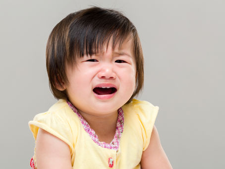 Crying child in a yellow shirt against a gray background, appearing upset and distressed. Joyful Seeds Paediatric and Developmental Clinic located in Bukit Timah