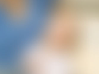 Baby in white outfit drooling, held by person in blue textured top. Neutral background. Calm expression. Joyful Seeds Paediatric and Developmental Clinic located in Bukit Timah