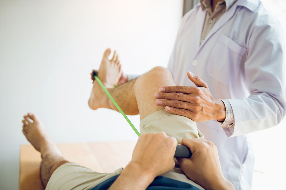 A physiotherapist wearing a white clinical coat guides a patient through a knee rehabilitation exercise using a green resistance band on a treatment table.